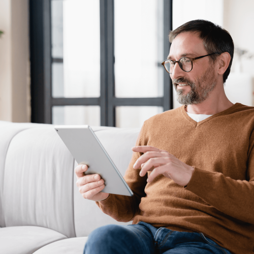 Smiling middle-aged man with beard sitting on couch with tablet in his hands