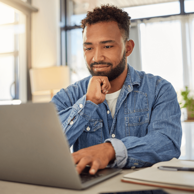 Young man in blue denim jacket sitting at desk using a laptop